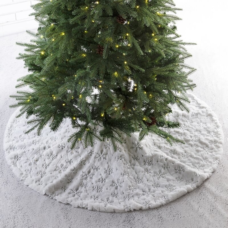 White tree skirt with silver snowflakes on it under tree