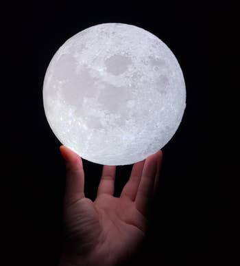 Reviewer's hand holding the lit moon lamp