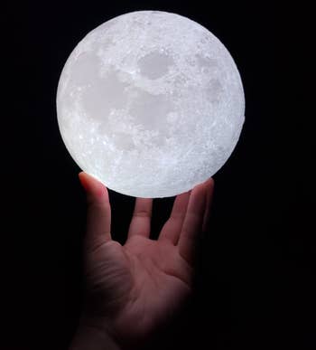 Reviewer's hand holding the lit moon lamp