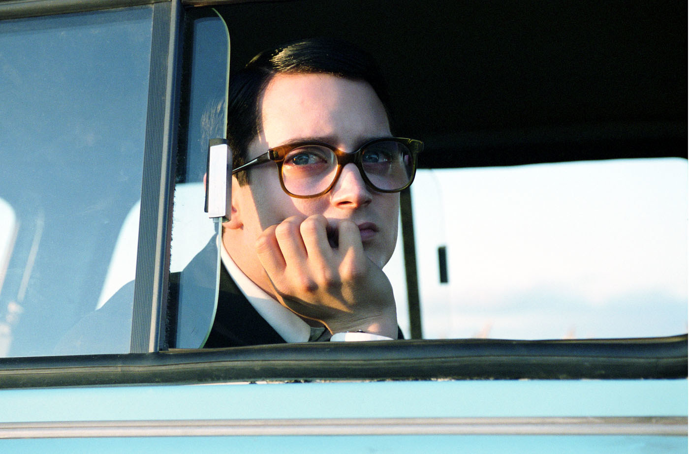Elijah Wood wearing glasses, looking out a car window