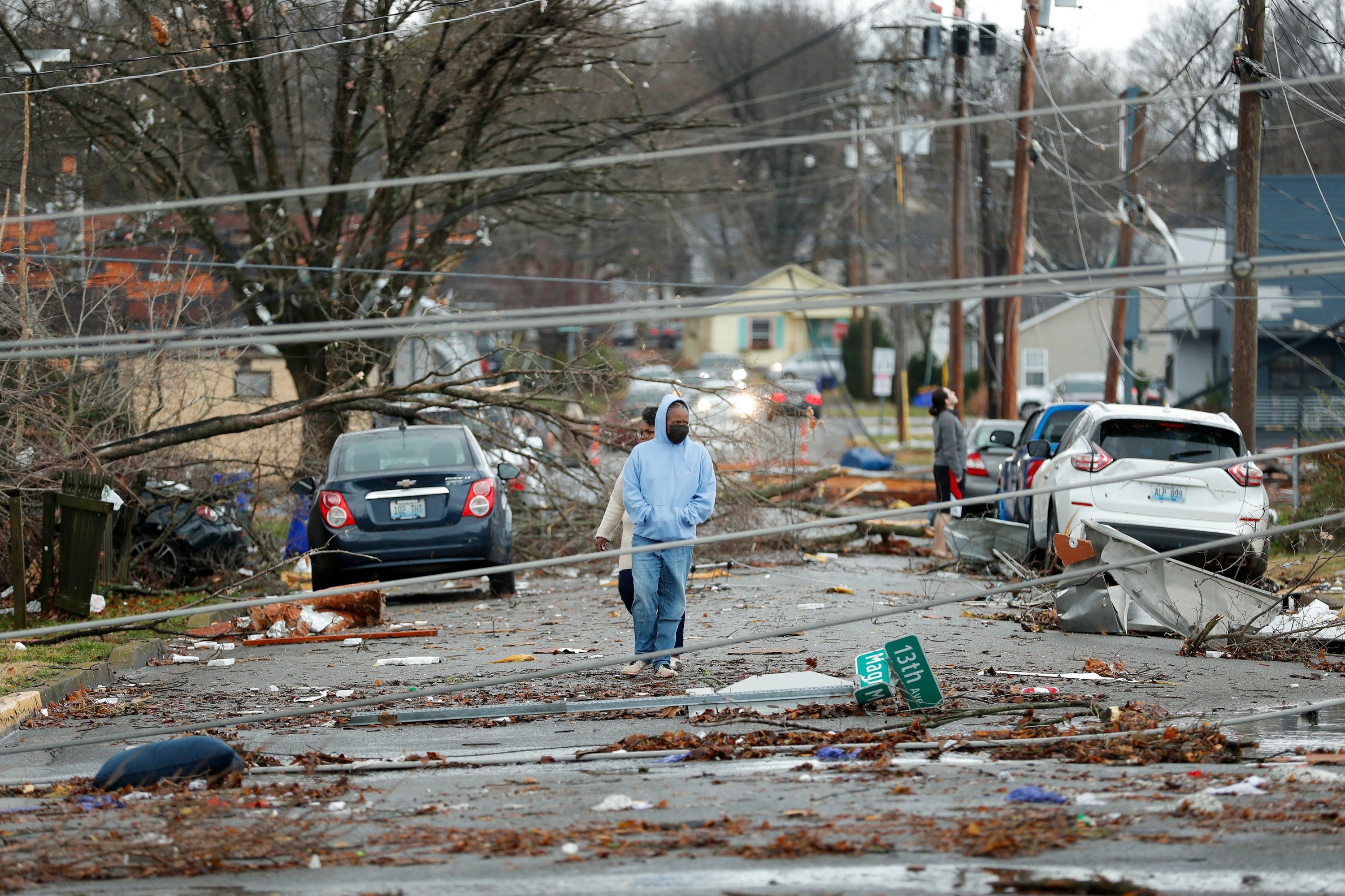 People walk between cars and debris, including fallen street signs