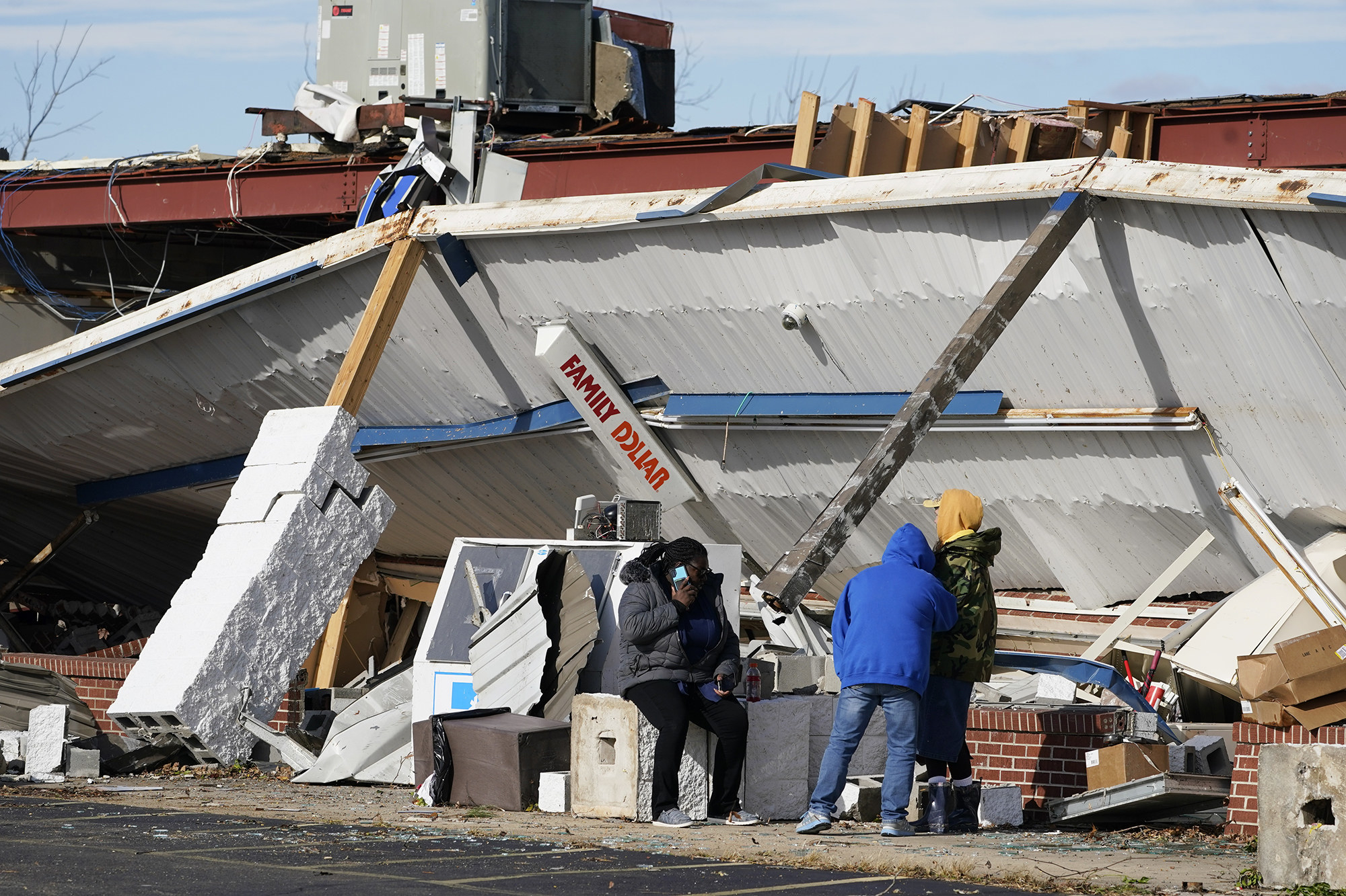 A &quot;Family Dollar&quot; sign is seen on a collapsed awning as people sit and stand nearby