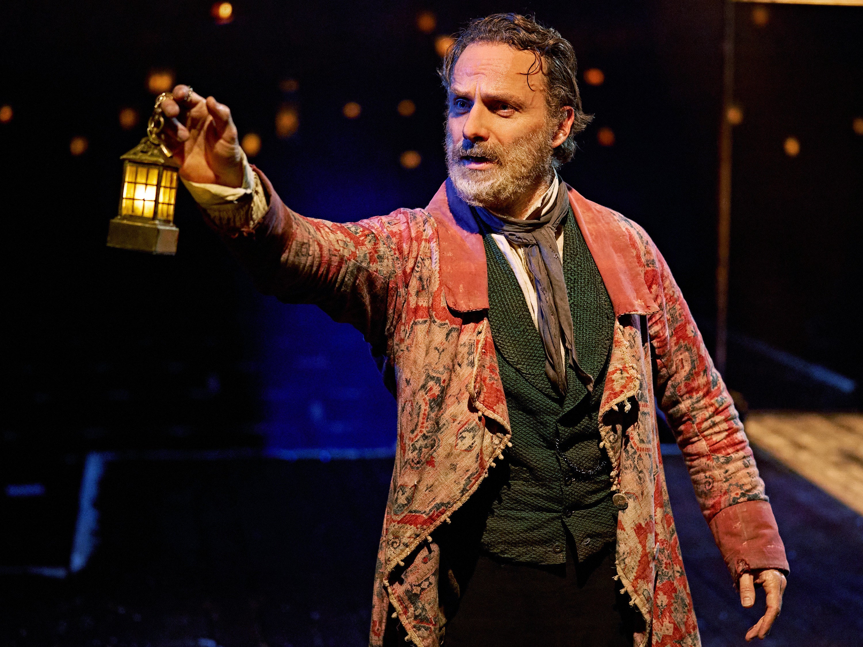 Andrew Lincoln on stage holding a small lamp pointing towards the audience