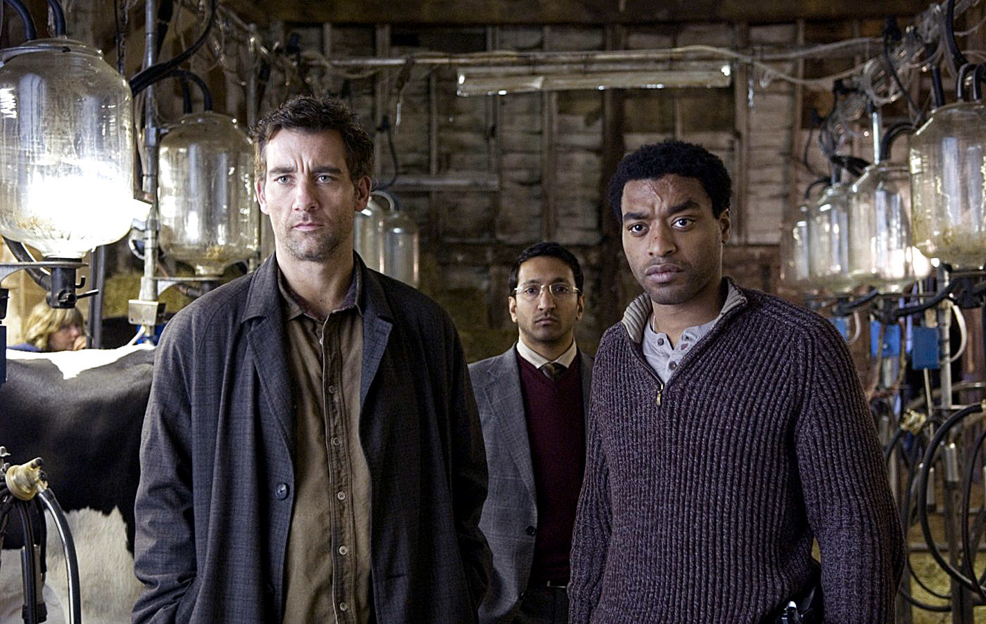 Clive Owen, Paul Sharma, Chiwetel Ejiofor, standing in a barn full of cows attached to jars