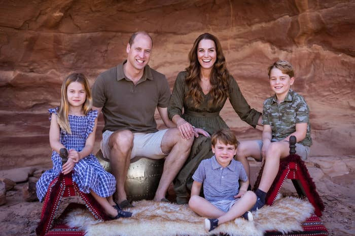 The Duke and Duchess of Cambridge and their three children smile while sitting amid a rocky setting