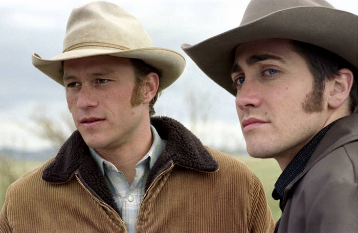 Heath Ledger and Jake Gyllenhaal look in the distance in cowboy outfits