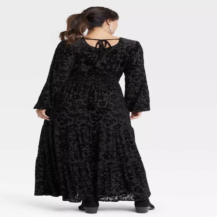 back view of model wearing the dress in a black velour design, showing off the tie in the back