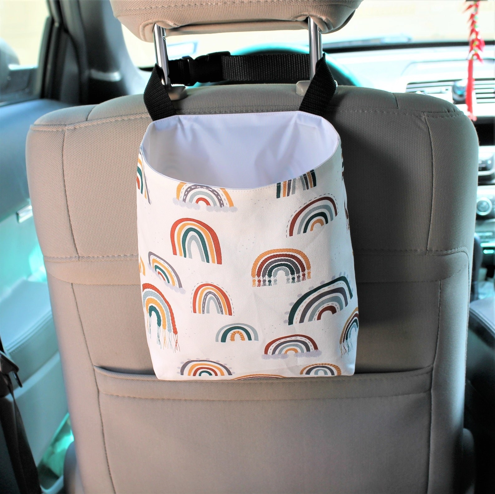 The trash can hooked behind the passenger seat with a boho rainbow pattern on it