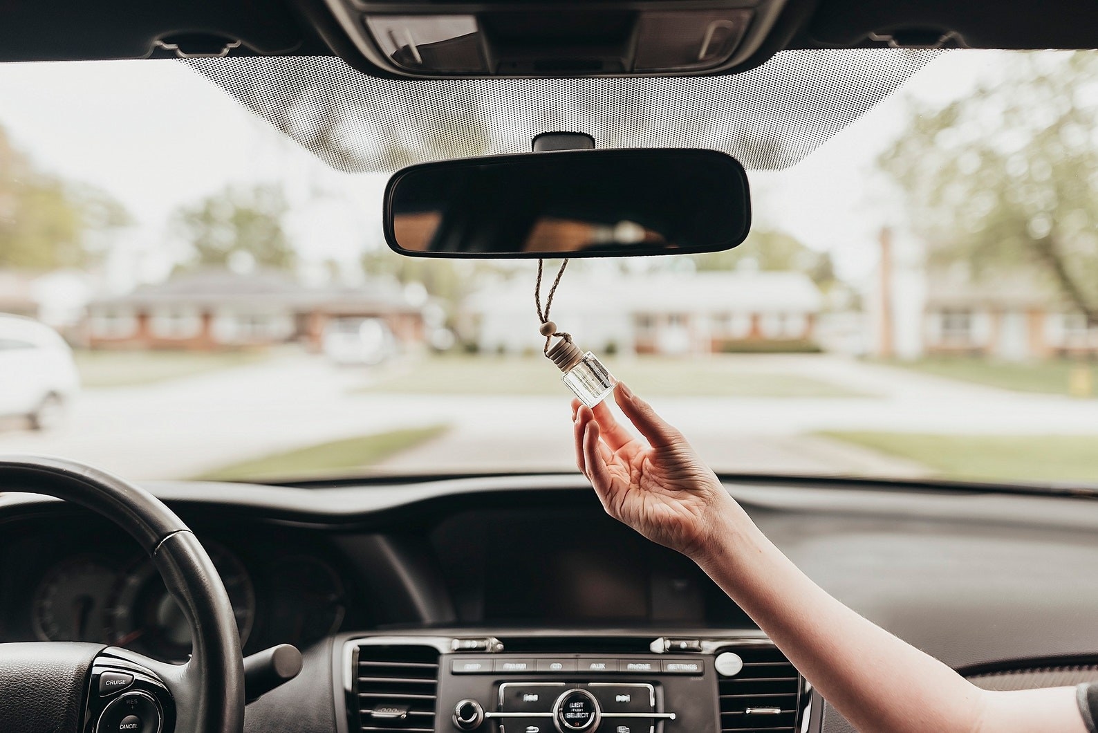 Model is holding the diffuser in their hand as it hangs off a rear view mirror in a car