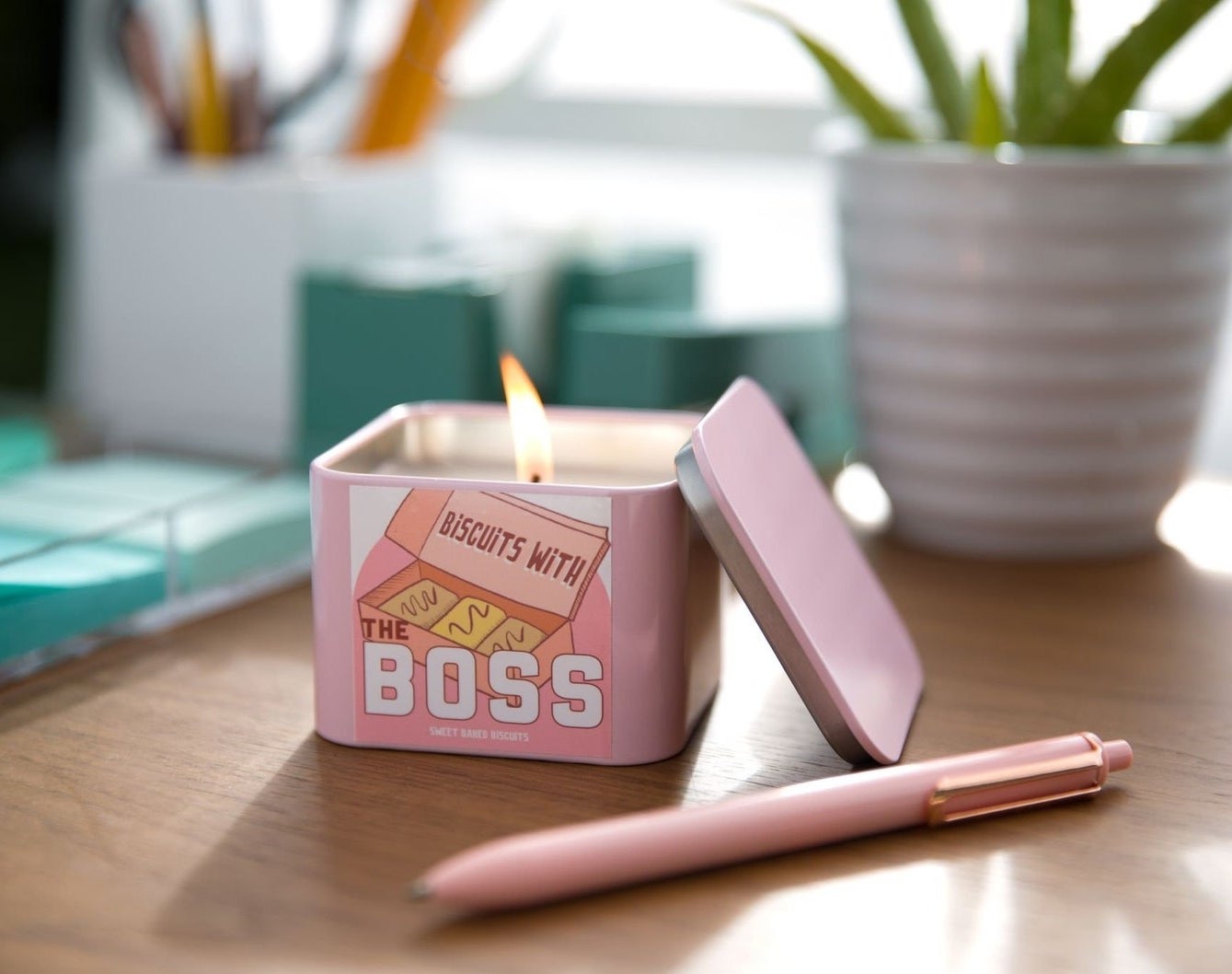 The pink biscuits with the boss candle lit up, on a desk surrounded by office accessories