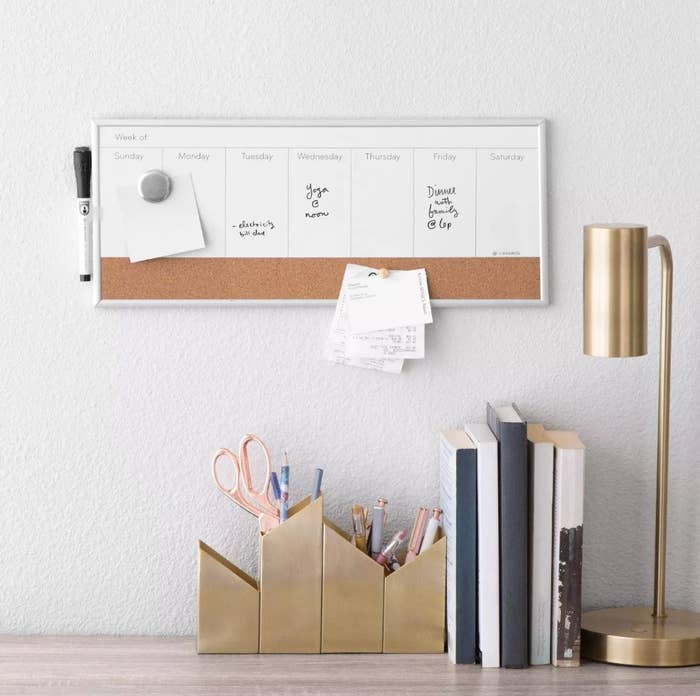 Dry erase calendar on wall above desk with books lamp and pencil holders