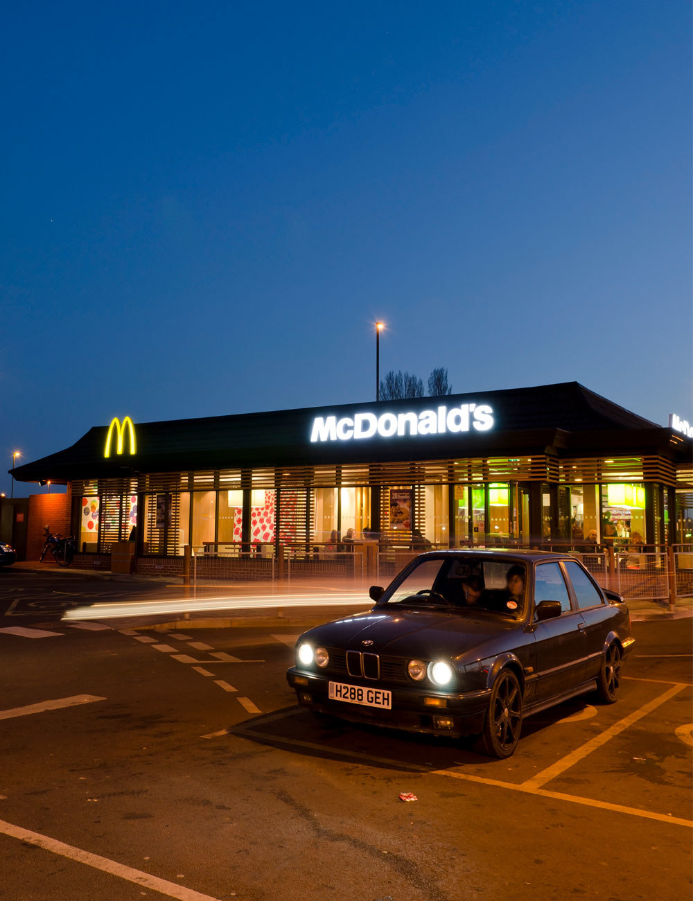 A car in a McDonald&#x27;s parking lot at night.