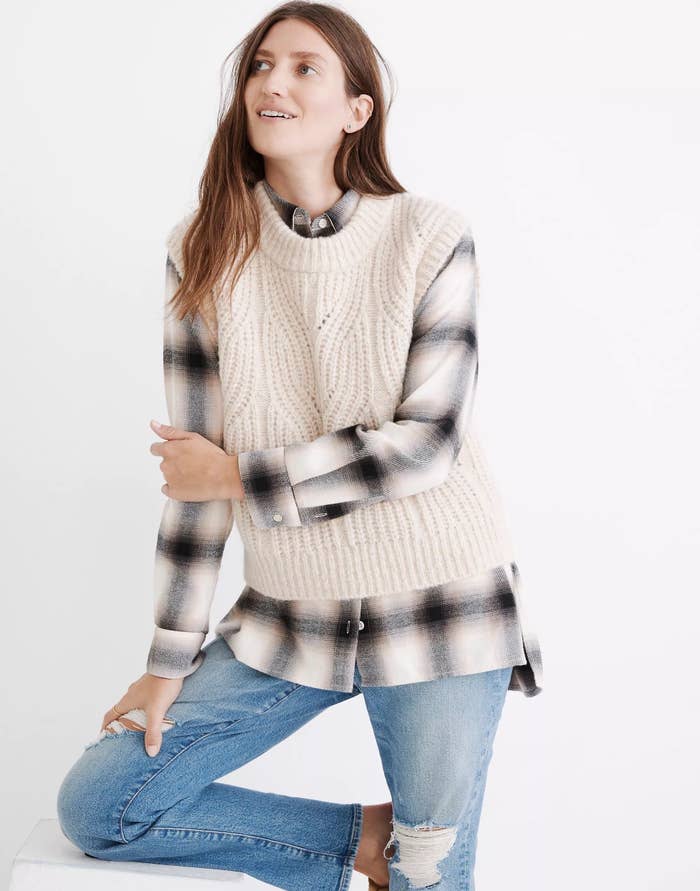 Model wearing white sweater vest over flannel with jeans