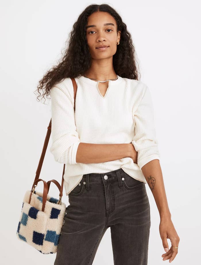 Model wearing white top with black jeans and colorful bag