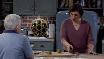A woman with two friends around her angrily slices a lime in half on a chopping board.