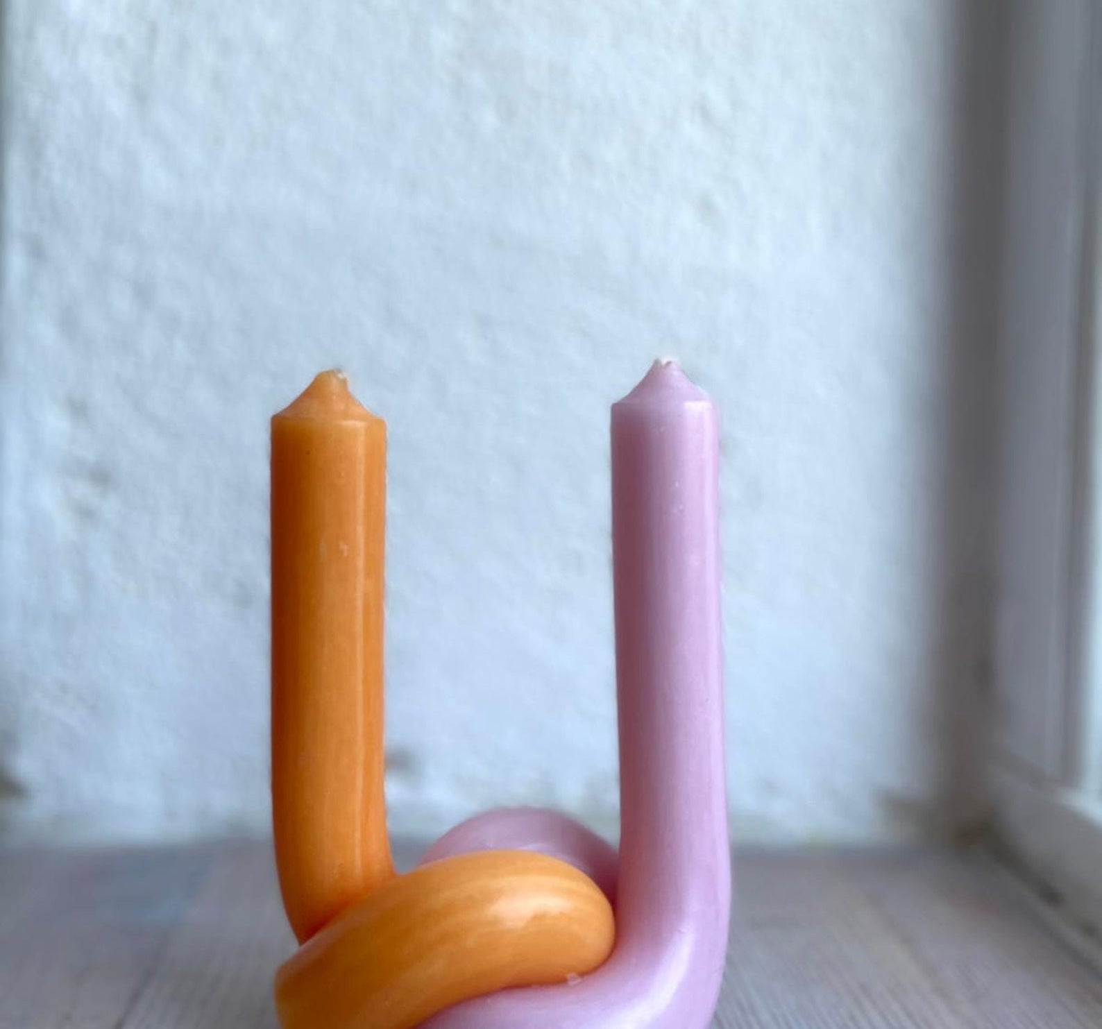 one orange and one pink candle stick twisted together at the base