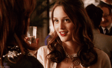 A close up of Blair Waldorf as she fake smiles at someone while holding a glass of champagne