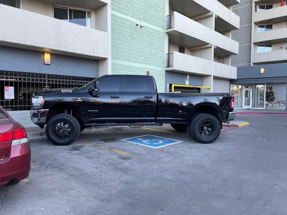 A truck parked over three spaces including a disabled spot, an emergency vehicle spot, and a 10 minute delivery spot