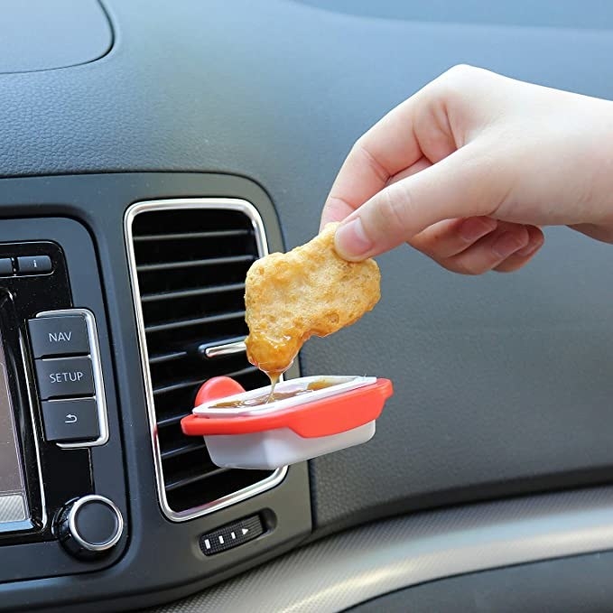 A person&#x27;s had dipping a chicken nugget into sauce clipped to an air vent in a car