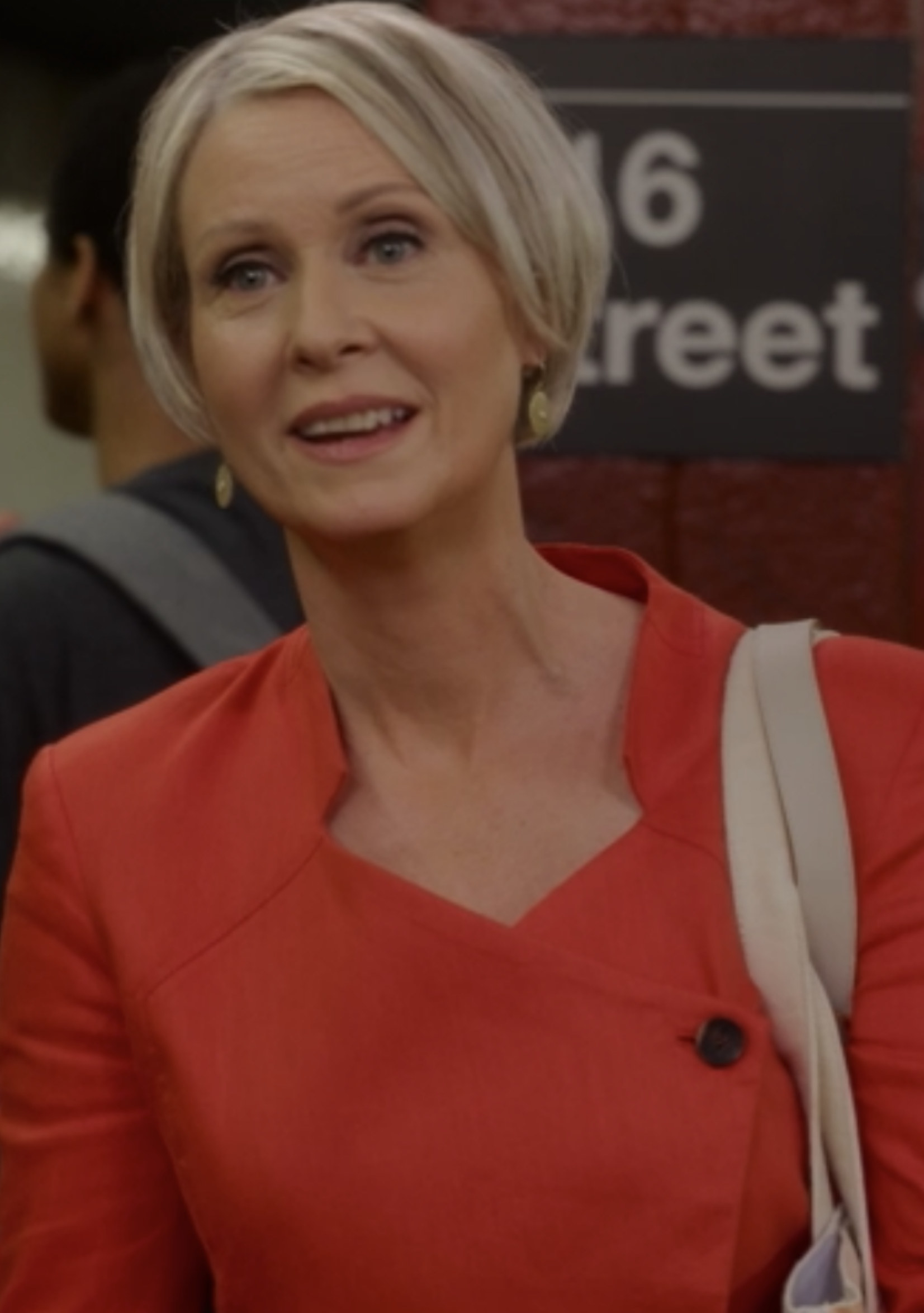 Nixon wearing a bright-colored suit dress, standing on the subway platform