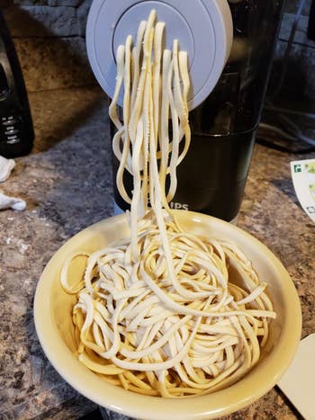 Reviewer photo of homemade noodles being extruded through the pasta maker and into a bowl
