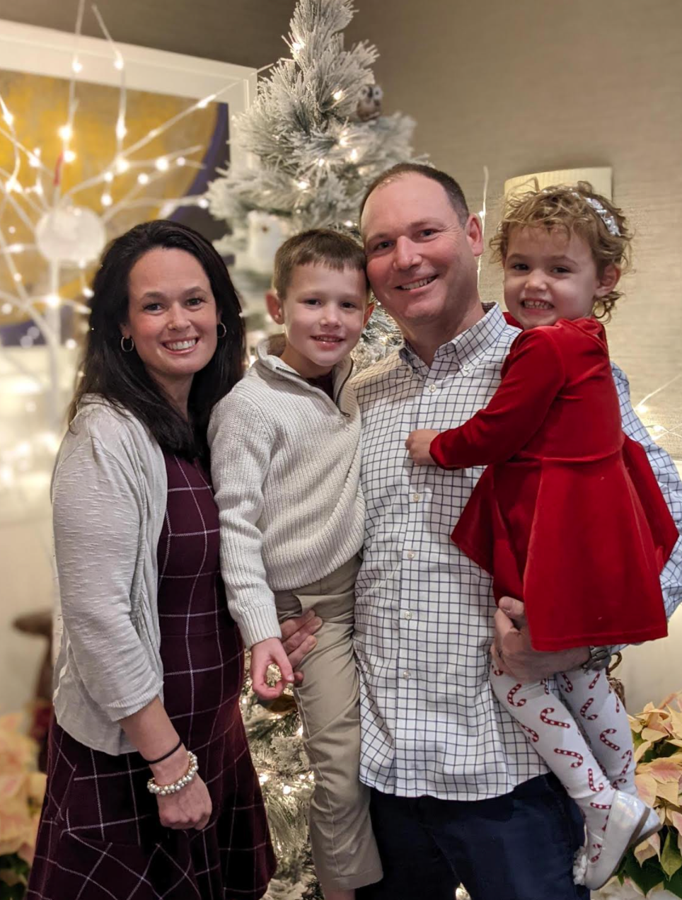 Lauren poses for a picture in front of a frosted Christmas tree with her family, including Peyton