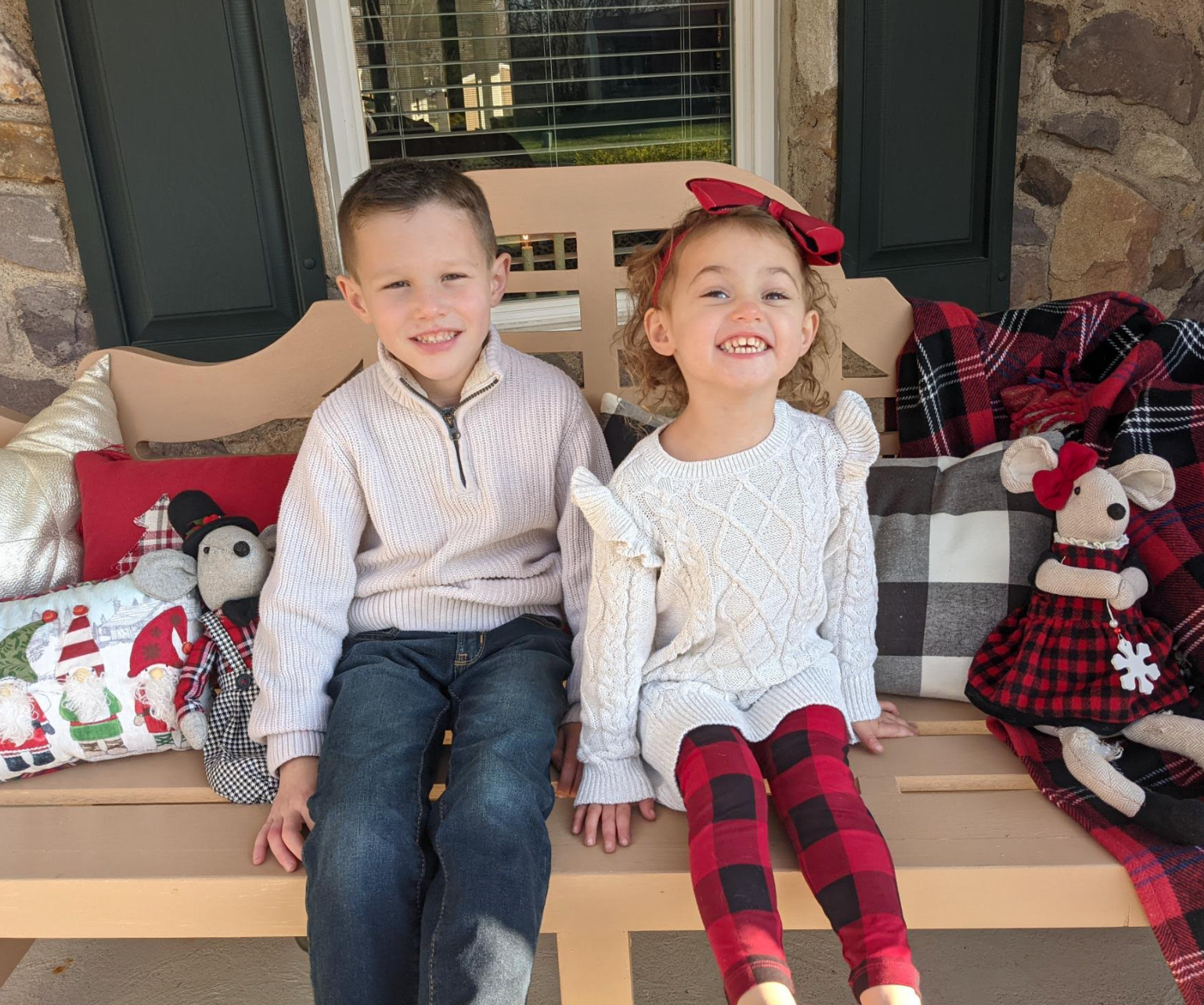 Lauren and her sibling sitting on a bench filled holiday-decorated pillows and stuffed toys