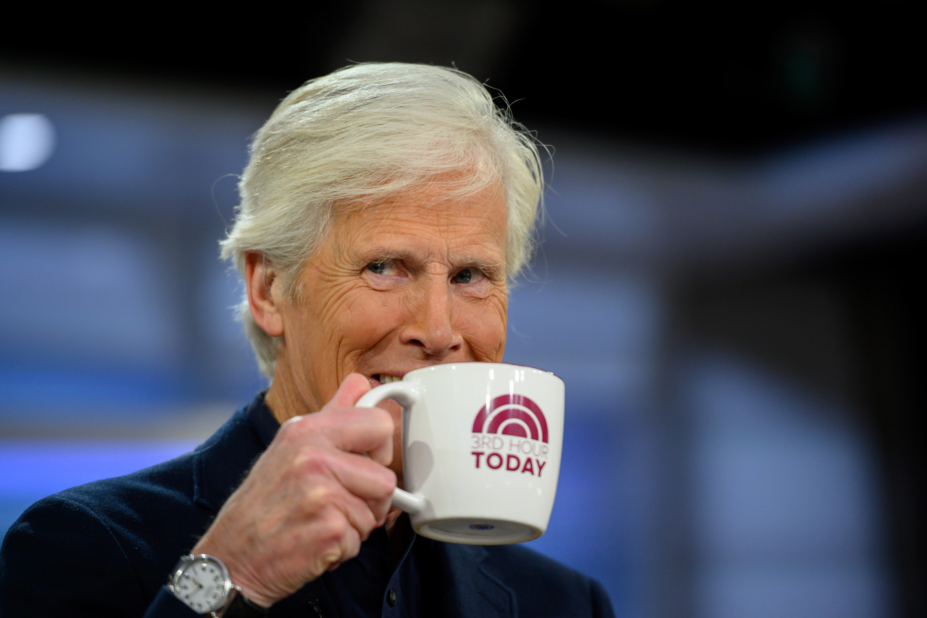 Keith Morrison grins and holds up a coffee cup on set.