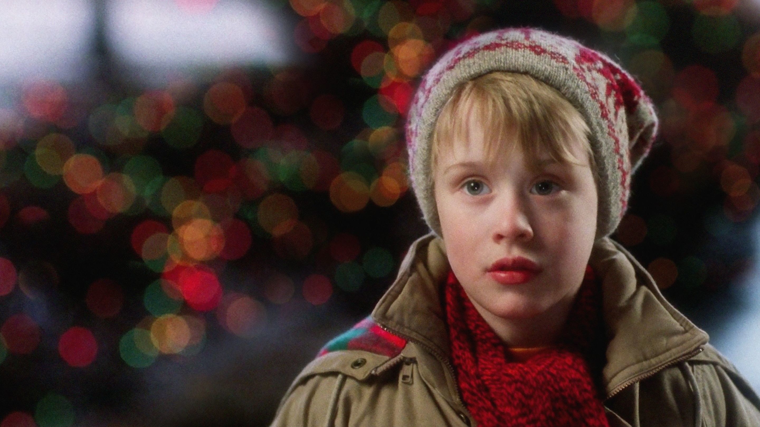 A shot from the movie Home Alone, with Macaulay Culkin dressed in a red scarf, brown jacket and a red winter hat.