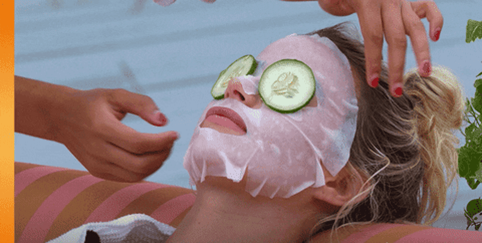 GIF of woman wearing sheet mask, with cucumbers over her eyes, getting a face massage