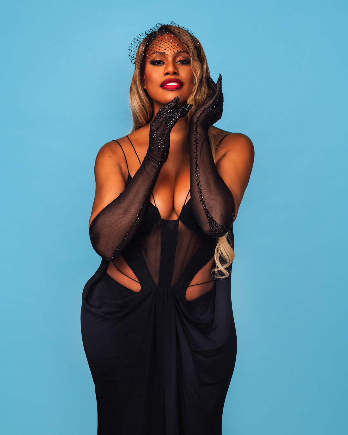 Laverne holds her hands up to her face in a seductive pose as she wears a partially see-through cutout dress