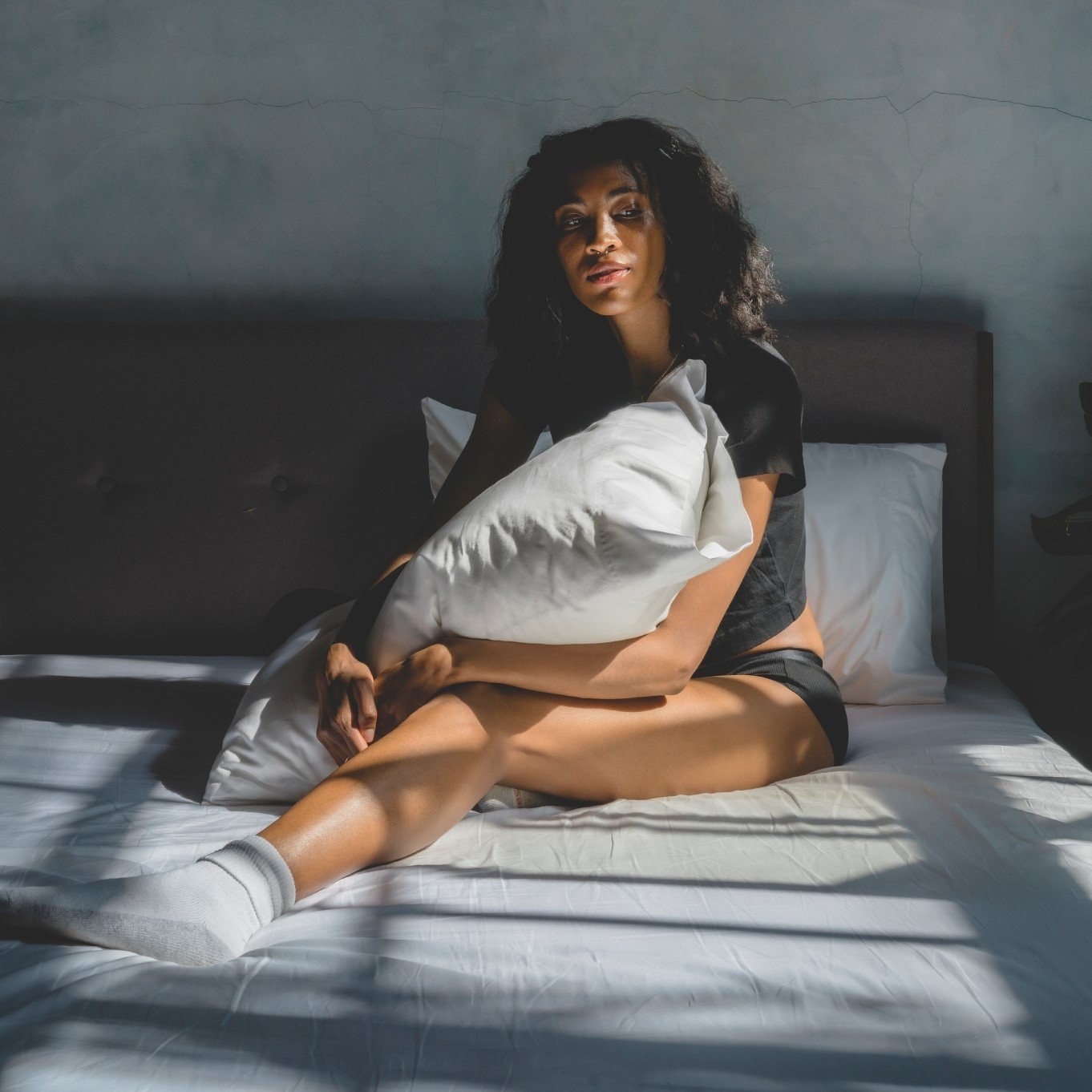 a model sitting on white sheets holding a pillow