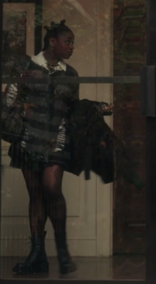 Shan Barnes wears a dark colored striped sweater dress with rips in it, sheer tights, and combat boots