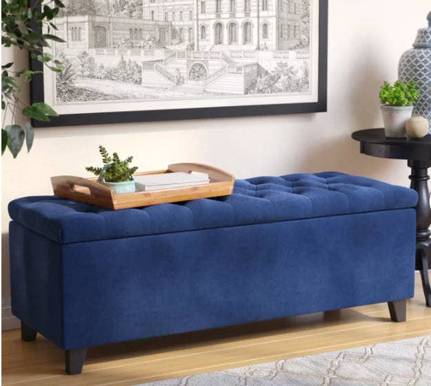 A velvet ottoman/storage bench with birch wood legs that opens at the top for storage