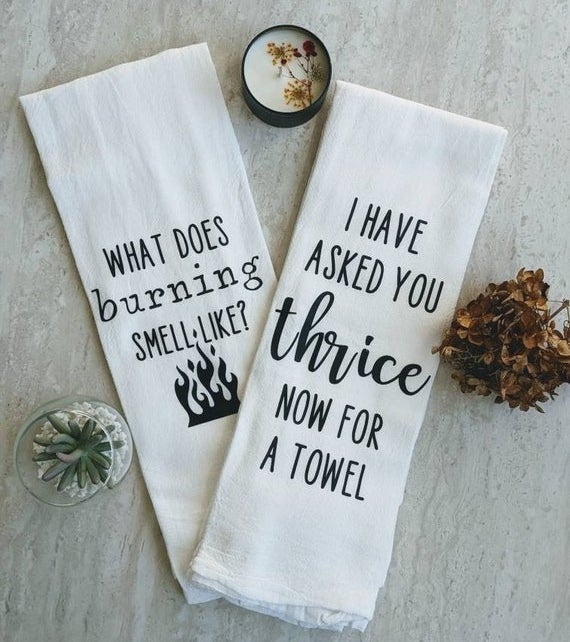 a white tea towel that says &quot;what does burning smell like?&quot; with a small flames icon and another that says &quot;I have asked you thrice now for a towel&quot;