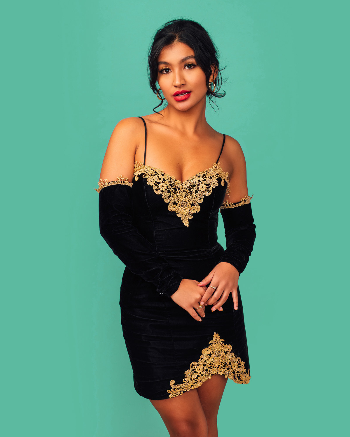Deja  has their hands clasped as they pose in a short lace and velvet dress