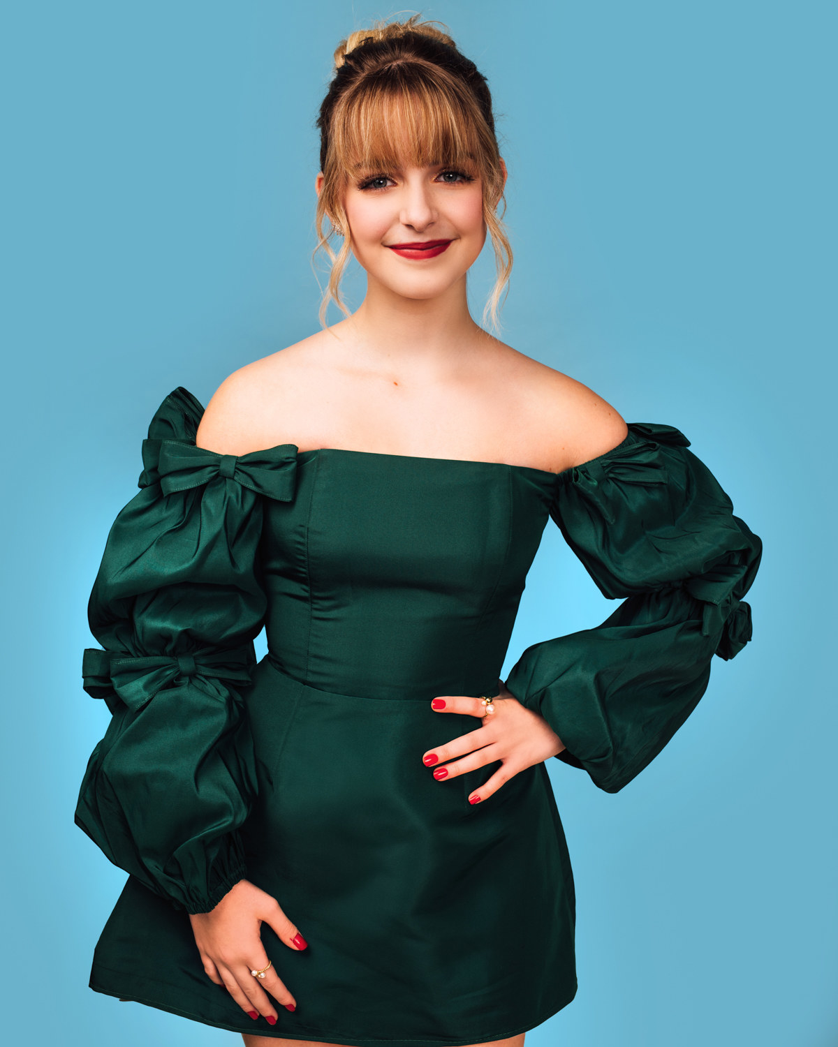 McKenna poses with her hand on her hip while wearing a short off-the-shoulder dress with long sleeves embellished with bows