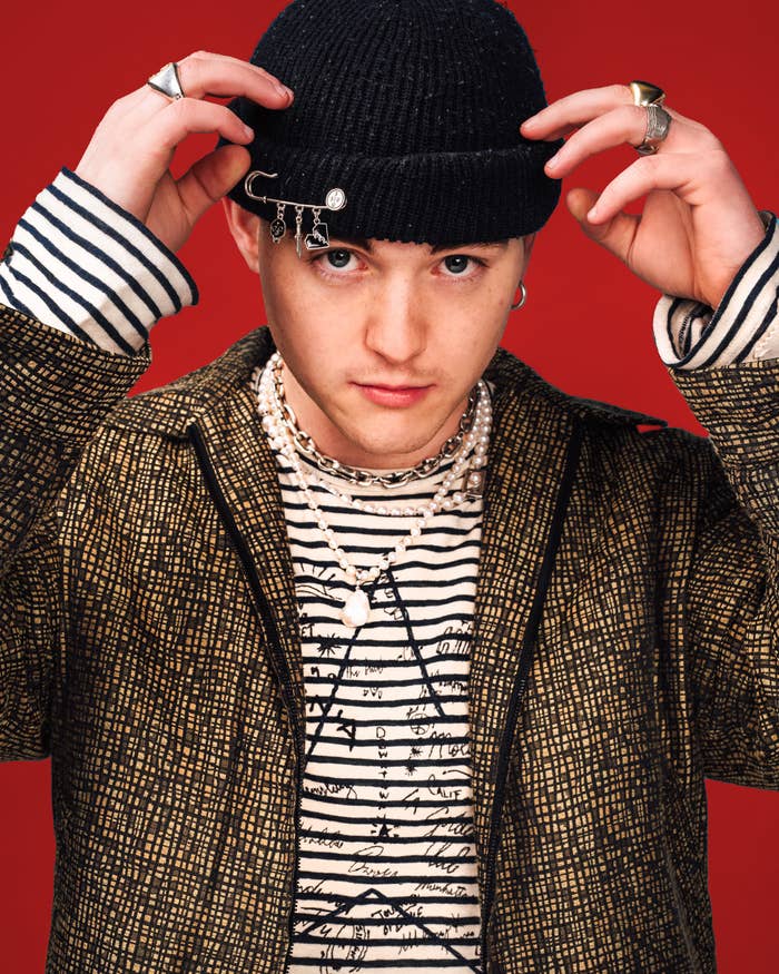 Trevor adjusting his beanie as he poses in a striped long-sleeved shirt and blazer