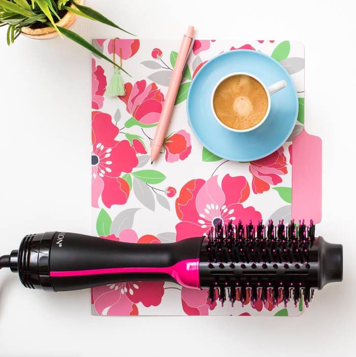 A blowdryer brush on top of a floral file folder, next to a cup of coffee