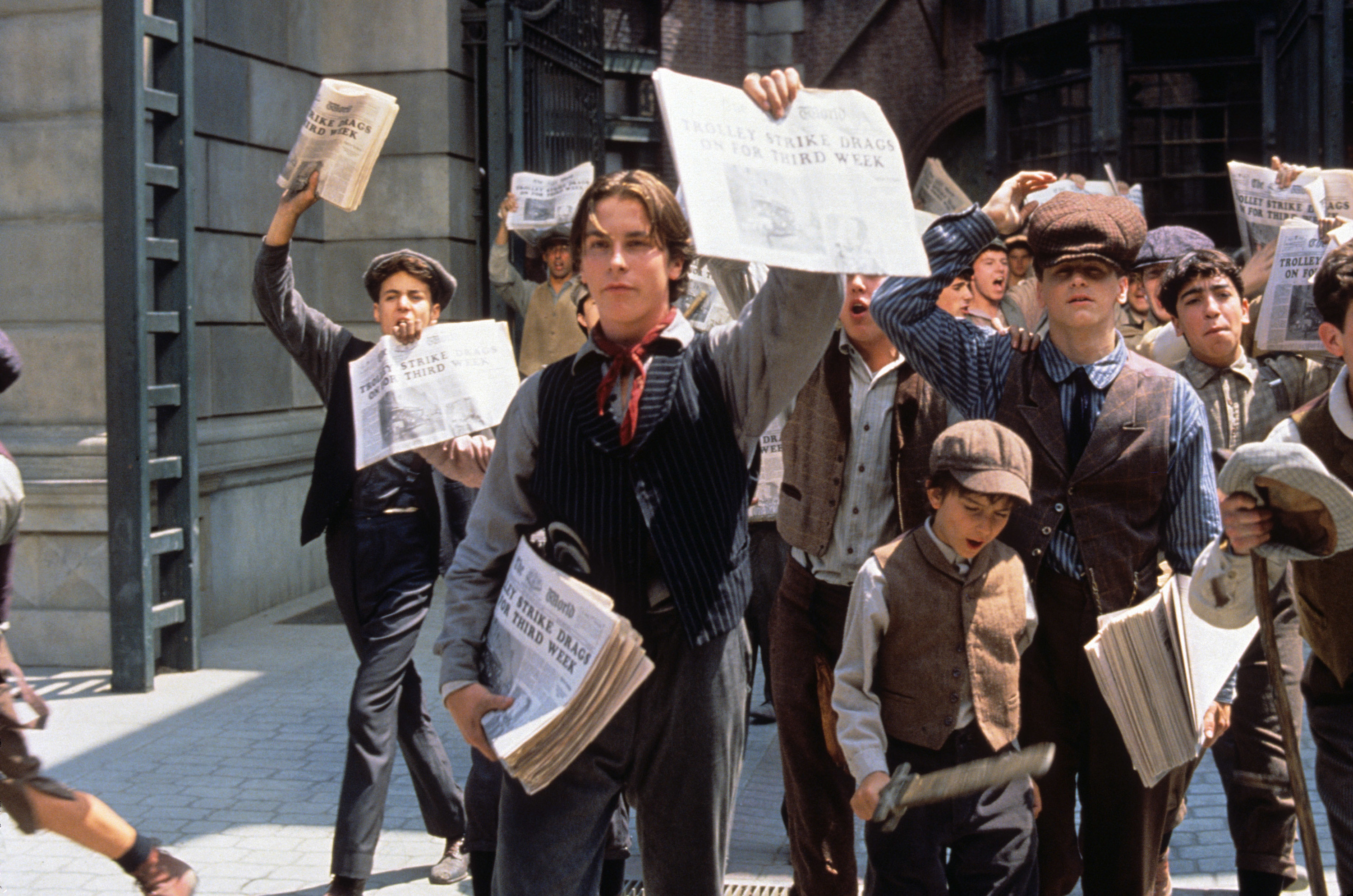 Christian Bale and the cast of Newsies selling newspapers
