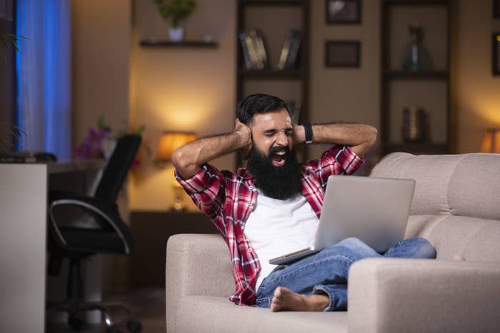 Man covering his ears in frustration while working on computer