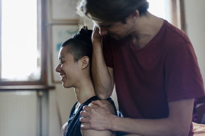 A partner gives their smiling partner a neck massage with their elbow