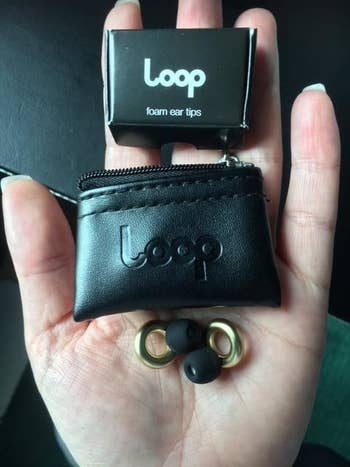 a reviewer shows the gold ear plugs and packaging out on the palm of their hand
