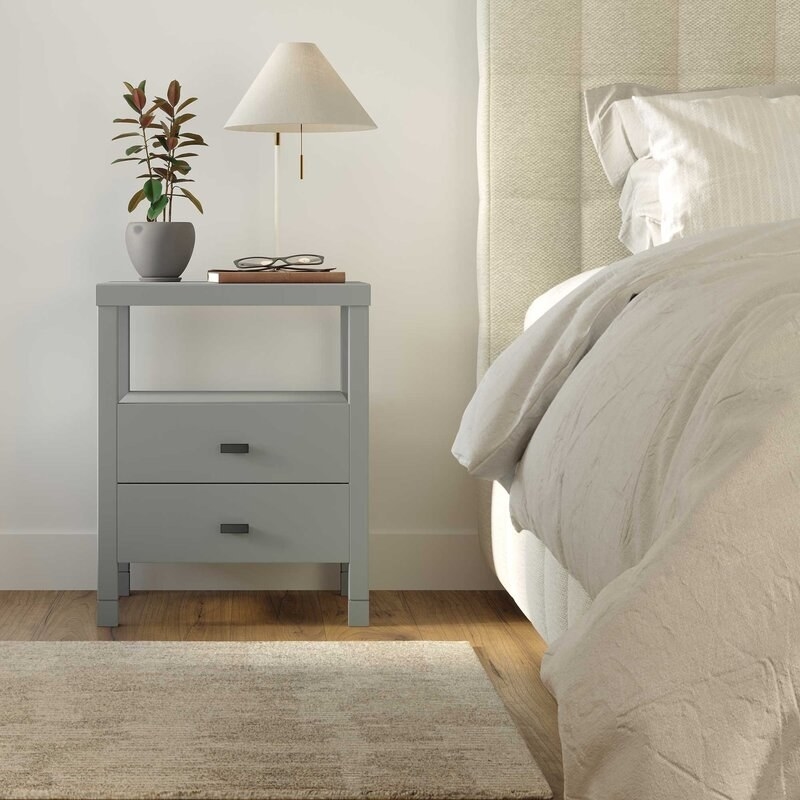 Gray nightstand with a lamp and a plant, next to a bed