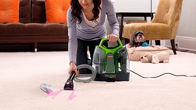 A person vacuuming up a stain on a carpet with a little rug cleaner