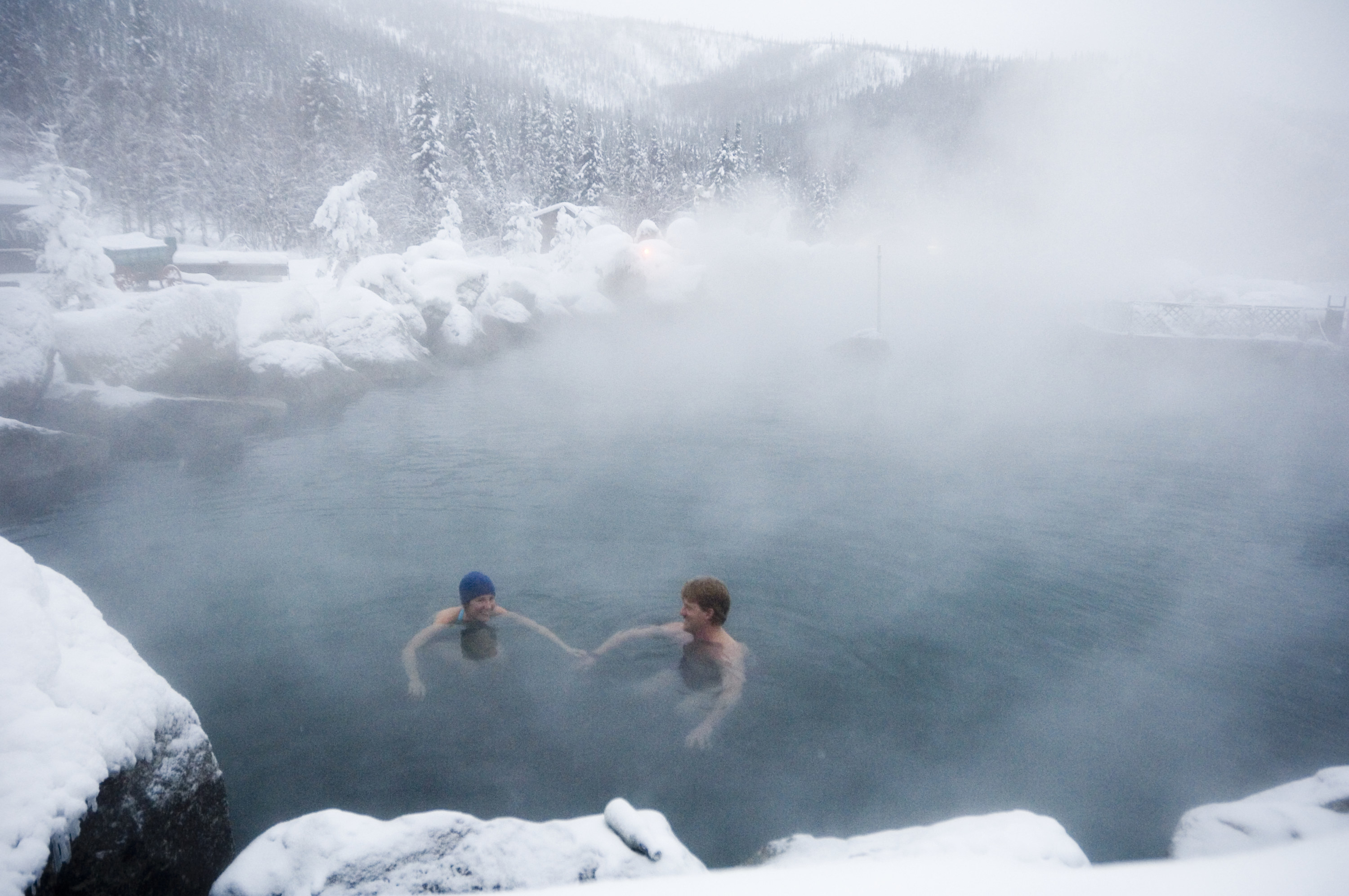 Two people swimming in a steamy outdoor pool surrounded by snow