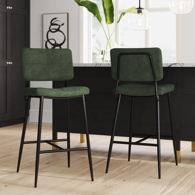 the two black metal stools with green cushions