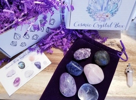 The Cosmic Crystal Box next to six assorted stones, a crystal pendant, and an identification card
