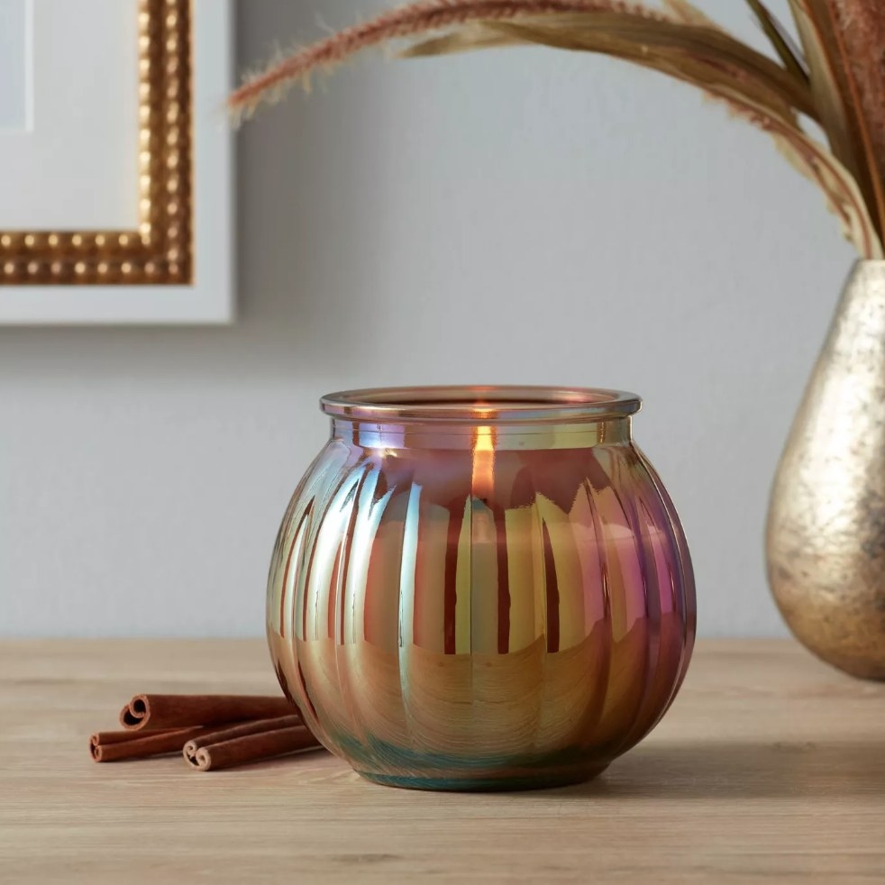 Copper iridescent candle jar sitting on wooden table next to sticks of cinnamon