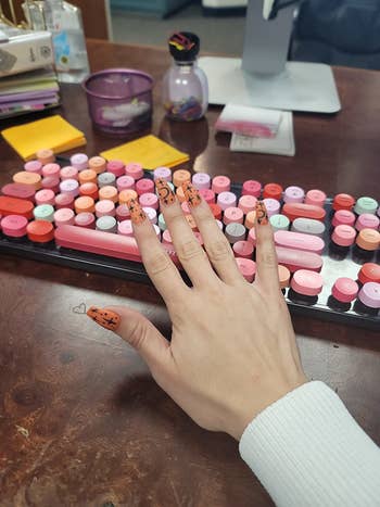 reviewer holds manicured hand in front of pink, orange, and red colorful keyboard